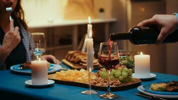 cerca arriba de joven hombre torrencial rojo vino en esposa vaso. romántico caucásico contento Pareja sentado a el mesa en cocina celebrando con vela luces, amor y aniversario. romance sorpresa en relación foto