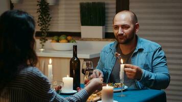 Couple eating and drinking wine with man in foreground during festive dinner in the kitchen. Talking happy sitting at table dining room, enjoying the meal at home having romantic time at candle lights photo