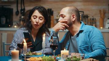 joven esposa demostración fotos en teléfono inteligente a su marido durante romántico cena. Pareja sentado a mesa hablando utilizando teléfono hojeada buscando Internet tecnología surf en línea celebrando aniversario