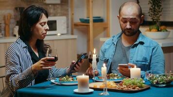 enfocado casado Pareja leyendo Noticias de Los telefonos durante romántico cena. adultos sentado a el mesa, hojeada en línea, surf, utilizando teléfonos inteligentes, celebrando su aniversario en el comida habitación. foto