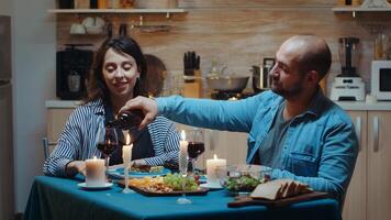 relajado joven marido hablando con su esposa y torrencial rojo vino en lentes. romántico caucásico contento Pareja sentado a el mesa en cocina celebrando matrimonio a vela luces, amor y aniversario foto