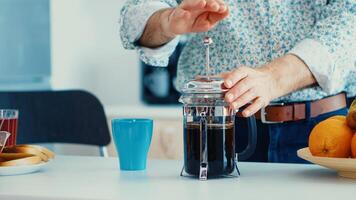 antiguo hombre emprendedor abajo el tapa de francés prensa mientras haciendo café para desayuno en cocina. mayor persona en el Mañana disfrutando Fresco marrón café Café exprés taza cafeína desde Clásico taza, filtrar relajarse refresco foto