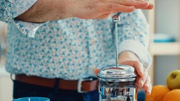 Senior man preparing coffee using french press in kitchen for breakfast. Elderly person in the morning enjoying fresh brown cafe espresso cup caffeine from vintage mug, filter relax refreshment photo