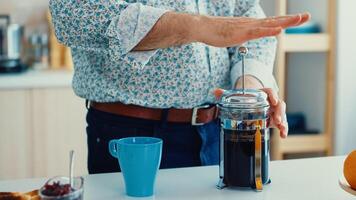 Senior man making coffee using french press during breakfast in kitchen. Elderly person in the morning enjoying fresh brown cafe espresso cup caffeine from vintage mug, filter relax refreshment photo