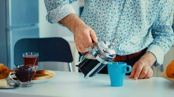 Senior man using french press for coffee preparation and pouring it in mug. Elderly person in the morning enjoying fresh brown cafe espresso cup caffeine from vintage mug, filter relax refreshment photo