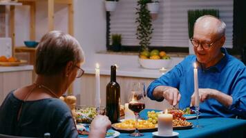 antiguo maduro Pareja comiendo durante romántico cena sentado a el mesa en el moderno cocina. alegre mayor antiguo personas hablando, disfrutando el comida, celebrando su aniversario en el comida habitación. foto