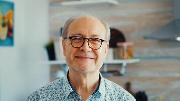 Close up of smiling senior man in kitchen looking at camera wearing eyeglasses. Portrait of relaxed elderly older person in the morning, enjoying fresh warm drink. Healthy smiling adult face photo