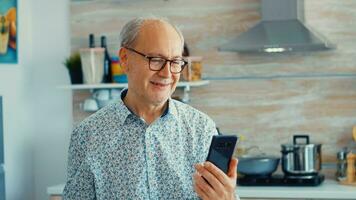 Elderly aged man waving during a video conference with family in kitchen. Elderly person using internet online chat technology video webcam making a video call connection camera communication conference call photo