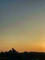 un puesta de sol terminado un ciudad con aves volador en el cielo foto