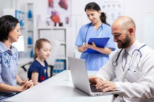 Pediatrician doctor and nurse sitting at desk in medical office talking with child. Healthcare practitioner specialist in medicine providing professional radiographic treatment in hospital clinic photo