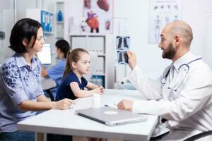 Pediatrician examining sick child radiography during medical consultation. Healthcare physician specialist in medicine providing health care services treatment examination. photo