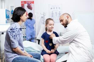 Doctor listening lungs of sick girl using stethoscope in hospital room during consultation. Healthcare physician specialist in medicine providing health care services treatment examination. photo