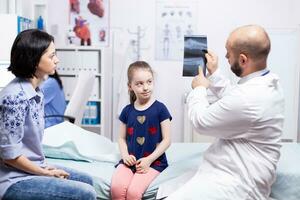 Doctor with mother and child looking at radiography in hospital office. Healthcare physician specialist in medicine providing health care services treatment examination. photo