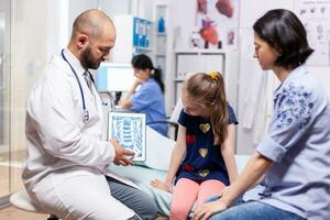 Physician showing on tablet digital xray talking with patients during appointment in medical clinic. Practitioner specialist in medicine providing professional treatment services photo