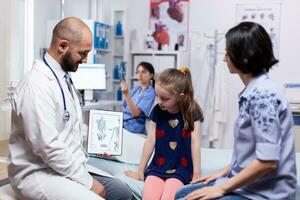 Doctor talking about diagnosis with mother of sick child in hospital office. Healthcare physician specialist in medicine providing health care services treatment examination. photo