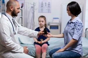 pediatra dando pastillas botella a madre de enfermo niño después consulta en hospital oficina. cuidado de la salud médico especialista en medicina Proporcionar salud cuidado servicios tratamiento examen. foto