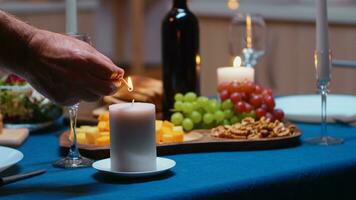 Elderly retired man lighting the candle waiting his wife for romantic dinner. Senior husband preparing festive meal with healty food for anniversary celebration, sitting near the table in kitchen. photo