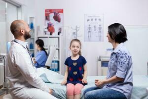 enfermo niño sonriente a madre durante médico examen en hospital oficina. cuidado de la salud médico especialista en medicina Proporcionar salud cuidado servicios tratamiento examen. foto