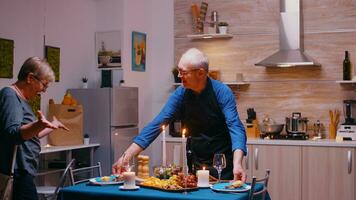 mayor marido sorprendente su esposa con romántico cena. mayor antiguo Pareja hablando, sentado a el mesa en cocina, disfrutando el comida, celebrando su aniversario con saludable alimento. foto