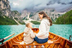 mujer con su hija sentado en grande marrón barco a lago di braies lago en nublado día, Italia. foto