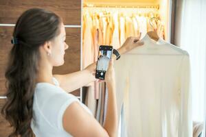 joven mujer tomando fotos de antiguo no deseado ropa para rebaja en teléfono inteligente aplicación