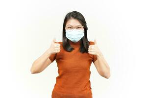 Wearing Medical Mask for Preventing Corona Virus And Showing Thumbs Up Of Beautiful Asian Woman Isolated On White Background photo