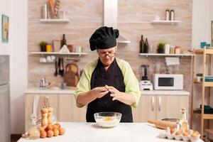 Chef hands with flour and eggs in preparation process for baking. Elderly pastry chef cracking egg on glass bowl for cake recipe in kitchen, mixing by hand, kneading. photo