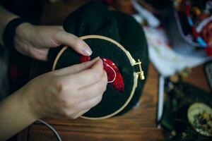 Women's hands embroiders fly agaric hat on frame. Wooden table with different objects on background. Concept of hobbies needlework and crafts. photo