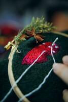 Woman hands doing stitch. Process of embroidery of mushroom hat in wooden hoop on green material. Concept of needlework diy, hobby, leisure. photo