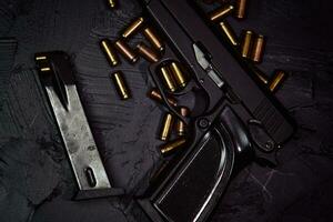 Flat lay of gun and cartridge with bullets. Weapons on concrete table. Pistol for defense or attack. Concept of crime ammunition and physical evidence. Firearms on dark background. photo