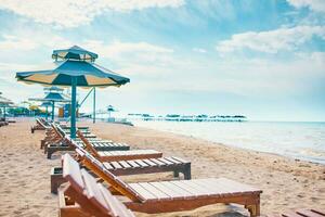 Sunbeds on the beach. A row of sun umbrellas with seats on the lake shore. photo