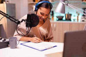 Influencer taking notes on clipboard while talking with followers during live on social media. Creative online show On-air production internet broadcast host streaming live content. photo