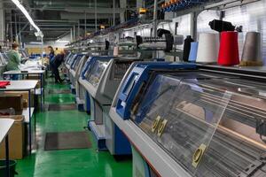 un fila de industrial textil plano tejido de punto máquinas en un prendas de punto fábrica. foto