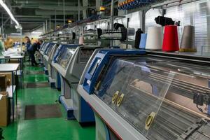 un fila de industrial textil plano tejido de punto máquinas en un prendas de punto fábrica. foto