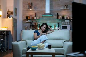 Caucasian lady asleep on sofa alone in living room while watching movie on tv late at home at night. Tired lonely housewife in pijamas falling asleep in front of TV sitting on comfortable couch. photo