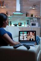 mujer persona de libre dedicación teniendo web charla conferencia sentado en sofá en vivo habitación. remoto trabajador que se discute a en línea reunión, consultante con colegas utilizando videollamada y cámara web trabajando en frente de ordenador portátil foto