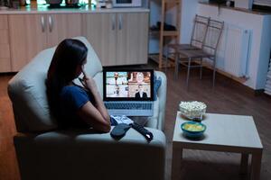 Woman speaking with colleagues on webcam lying on sofa at home. Remote worker having online meeting, video conference consulting with team using videocall working in front of laptop. photo