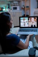 Back view of woman using laptop on videocall sitting on comfortable couch. Remote worker having online meeting consulting with colleagues on video conference and webcam chat using internet technology. photo