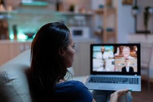 Freelancer having virtual conversation with colleagues on laptop sitting on couch in pijamas. Remote worker discussing during online meeting consulting with team on videocall using internet technology photo