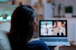 Lady participating at webinar sitting on sofa. Remote worker having online meeting, video conference consulting with colleagues on videocall and webcam chat working in front of laptop photo