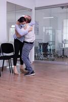 Happy young couple after receiving good from doctor wearing protection face mask in hospital waiting area hugging eatch other. Positive man and woman in clinic after test results during global pandemic photo