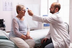 Medical staff using infrared thermometer to take old woman patient body temperature.Medical consultation for infections and disease during global pandemic,flu, tool, sickness. photo