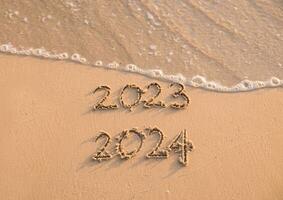 Handwritten inscription 2023 and 2024 on the beach in the sunset time. The concept of Goodbye 2023 and Happy New Year 2024 photo