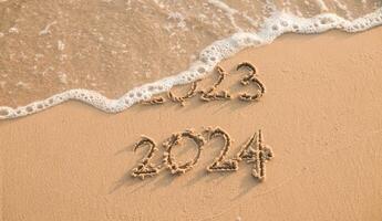 Handwritten inscription 2023 and 2024 on the beach in the sunset time. The concept of Goodbye 2023 and Happy New Year 2024 photo