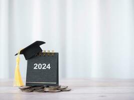 2024 desk calendar with graduation hat on stack of coins. The concept of saving money for education, student loan, scholarship, tuition fees in Year 2024 photo