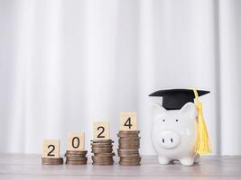 Study goals, Piggy bank with graduation hat and Wooden block with number 2024 on stack of coins. The concept of saving money for education, student loan, scholarship, tuition fees in New Year 2024 photo