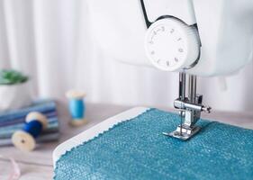 Cloe up sewing machine working with blue fabric, sewing accessories on the table, stitch new clothing. photo