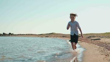 un' contento adolescente corre lungo il oceano riva spruzzi acqua con spoglio piedi. video