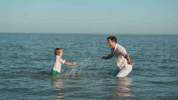 Father and son spray each other with water while swimming in the ocean. video