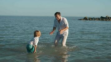 vader en zoon verstuiven elk andere met water terwijl zwemmen in de oceaan. video